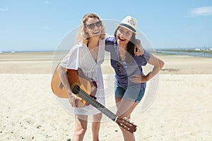 two jovial women on beach holding guitar