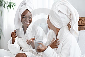 Two joyful black women joking while drinking tea