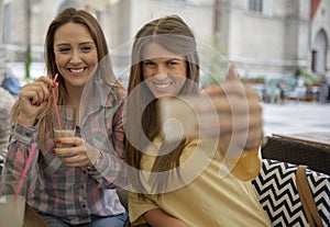 Two joyful cheerful girls taking a selfie while sitting at cafe