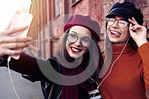 Two joyful cheerful girls taking a selfie while walking in the city street having fun.