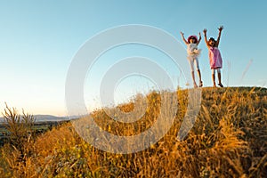 Two joyful children jumped and raised hands up - sunset after summer day. photo