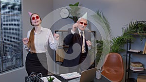 Two joyful collegues in formal suits dancing victory dance, celebrating success of business project