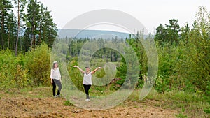 Two joyful girls friends of an Asian Yakut stand on a mountain slope in the taiga forest
