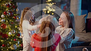 Two joyful girls playing with mother near christmas tree