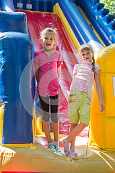 Two joyful girls stand at entrance to a large inflatable trampoline