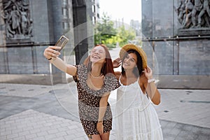 Two joyful girls taking a selfie on the city street