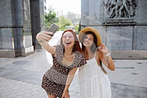 Two joyful girls taking a selfie on the city street
