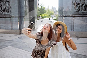 Two joyful girls taking a selfie on the city street