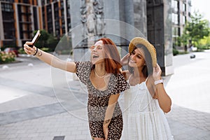 Two joyful girls taking a selfie on the city street