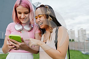 Two joyful girls using smartphone while standing outdoors