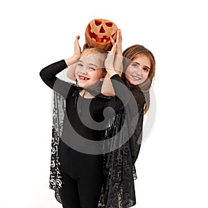 Two joyful girls in witch and vampire costumes play with pumpkin