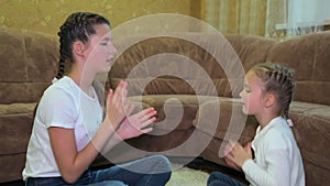 Two joyful happy Caucasian girls sisters play clapping their hands while sitting on the carpet near the sofa