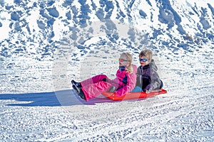 Two joyful kids sledding down the hills on a winter day.