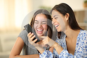Two joyful roommates laughing watching media on phone photo