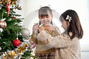 Two joyful young Asian girls are decorating a Christmas tree and celebrating Christmas together