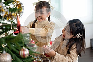 Two joyful young Asian girls are decorating a Christmas tree and celebrating Christmas together