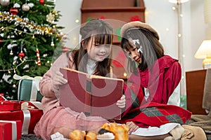 Two joyful young Asian girls are enjoying reading a Christmas fairy tale story in a book together