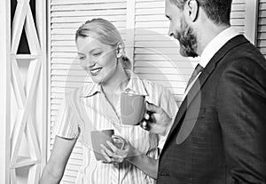 Two joyful young people in formalwear holding cups of coffee and discussing something while working together. Young