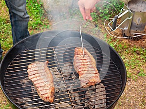 Two juicy beef steaks are grilled on a round grill. Meat readiness check