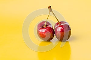 Two juicy berries of a red cherry on a yellow background