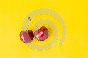 Two juicy berries of a red cherry on a yellow background