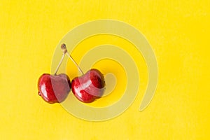 Two juicy berries of a red cherry on a yellow background