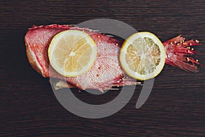 Two juicy lemon slices lie on fresh red fish. The fish is called sea bass.