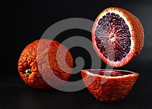 Two juicy ripe citruses - Sicilian red orange cut in half, located on a stone black background. Close-up