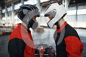 Two kart racers in helmets standing face to face