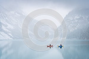 Two kayakers on azure alpine lake shrouded by mist during early winter, Banff N. Park, Canada