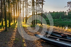 Two kayaks lie on the bank of the river, against the backdrop of the bright setting sun