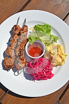 Two kebabs on skewers with a side dish of vegetable salads