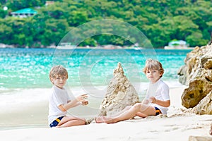 Two kid boys building sand castle on tropical beach