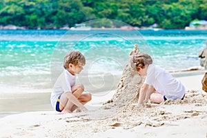 Two kid boys building sand castle on tropical beach