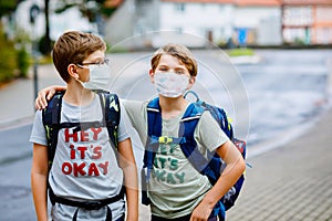 Two kid boys with medical masks and satchels. Schoolkids on the way to school. Children wear protective mask due to