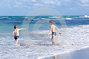 Two kid boys running on ocean beach. Little children having fun