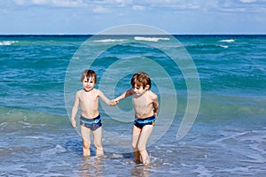 Two kid boys running on ocean beach. Little children having fun