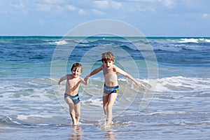 Two kid boys running on ocean beach. Little children having fun