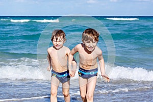 Two kid boys running on ocean beach. Little children having fun