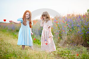 Two kid girls playing and dancing with wild flowers at summer da