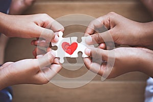 Two kid hands connecting couple jigsaw puzzle with drawn red heart