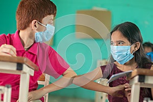 Two kid in medical mask at classroom greeting each other with elbow bumps while maintaining socail distance at school -