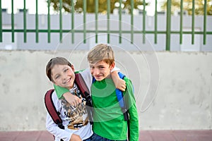 Two kids with backpacks on their backs hug each other looking at the camera. Back to school concept