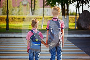 Two kids with backpacks walking on the road, holding. School tim