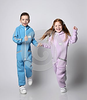 Two kids boy and girl in blue and pink jumpsuits with zippers and pockets are running towards camera holding hands