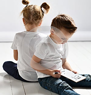 Two kids boy and girl in white t-shirts and blue jeans sit close to each other and play battleship