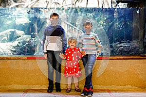 Two kids boys and toddler girl visiting together zoo aquarium. Three children watching fishes and jellyfishes. School