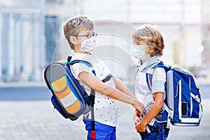 Two kids boys wearing medical mask on the way to school. Children with satchels. Schoolkids on warm sunny day. Lockdown