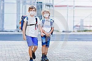 Two kids boys wearing medical mask on the way to school. Children with satchels. Schoolkids on warm sunny day. Lockdown