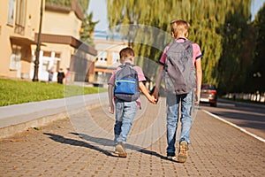 Two kids brothers with backpack holding on hands walking to school. Back view.